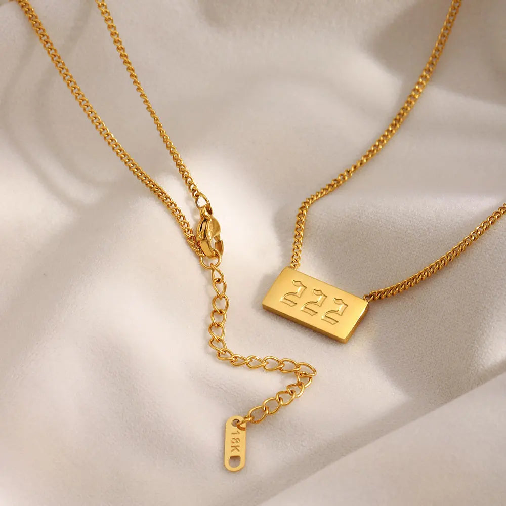 Two gold necklaces with engraved tags on a beige fabric background