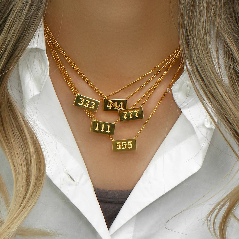 Gold necklaces with numbered pendants on a person wearing a white shirt.