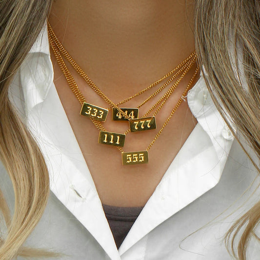 Gold necklaces with numbered pendants on a person wearing a white shirt.