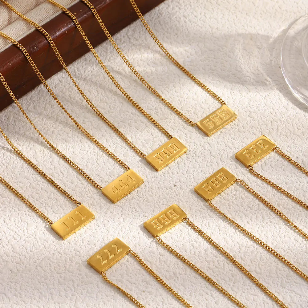 Gold necklaces with rectangular tags on a textured surface