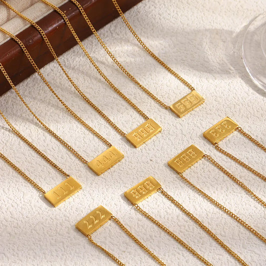 Gold necklaces with rectangular tags on a textured surface